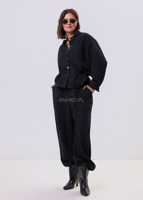Czarny kombinezon damski z długim rękawem, guzikami i elastyczną talią, stylizowany z czarnymi botkami.