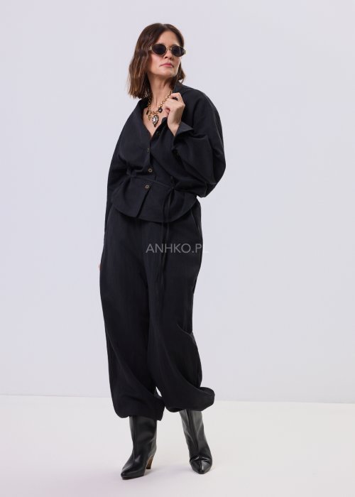 Czarny kombinezon damski z długim rękawem, guzikami i elastyczną talią, stylizowany z czarnymi botkami.