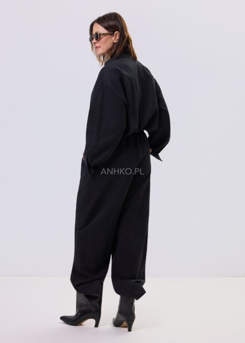Czarny kombinezon damski z długim rękawem, guzikami i elastyczną talią, stylizowany z czarnymi botkami.