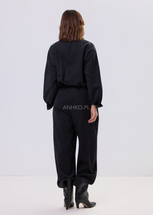 Czarny kombinezon damski z długim rękawem, guzikami i elastyczną talią, stylizowany z czarnymi botkami.