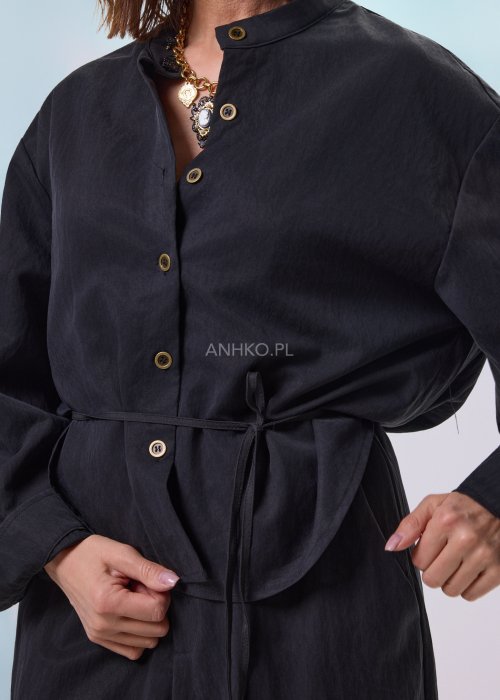 Czarny kombinezon damski z długim rękawem, guzikami i elastyczną talią, stylizowany z czarnymi botkami.