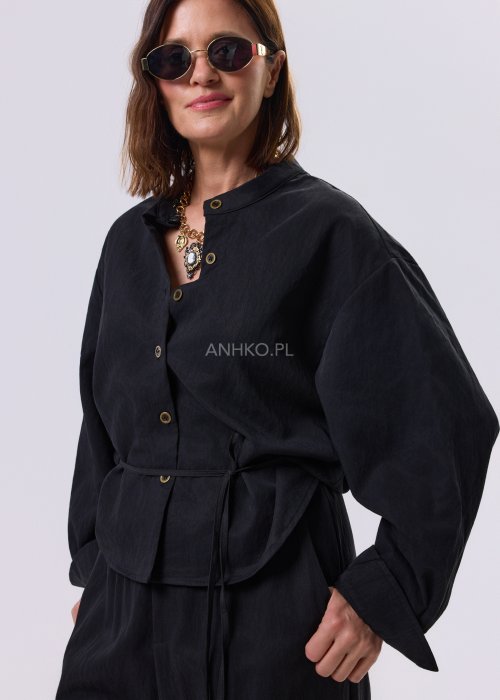 Czarny kombinezon damski z długim rękawem, guzikami i elastyczną talią, stylizowany z czarnymi botkami.