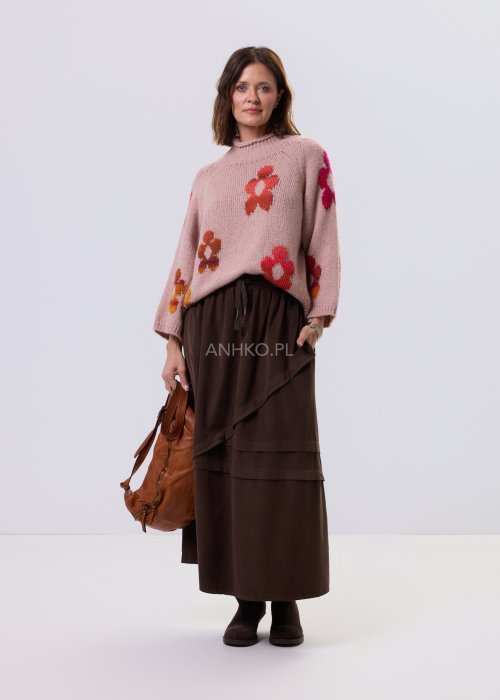 Pudrowo różowy sweter damski o luźnym kroju z dużymi, kolorowymi kwiatami w stylu retro, zestawiony z brązową spódnicą w casualowej stylizacji.