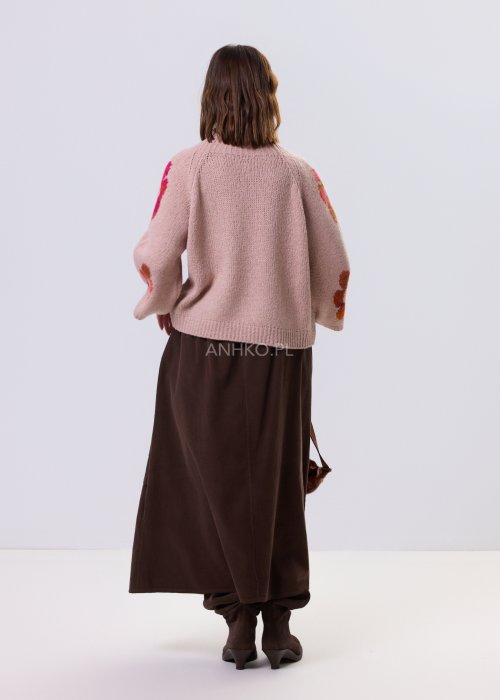 Pudrowo różowy sweter damski o luźnym kroju z dużymi, kolorowymi kwiatami w stylu retro, zestawiony z brązową spódnicą w casualowej stylizacji.