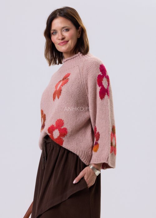 Pudrowo różowy sweter damski o luźnym kroju z dużymi, kolorowymi kwiatami w stylu retro, zestawiony z brązową spódnicą w casualowej stylizacji.