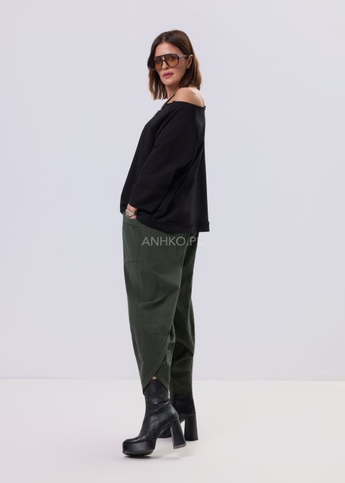 Czarna bluza damska o kroju oversize z raglanowymi rękawami, zestawiona z oliwkowymi spodniami i botkami w minimalistycznej, miejskiej stylizacji.