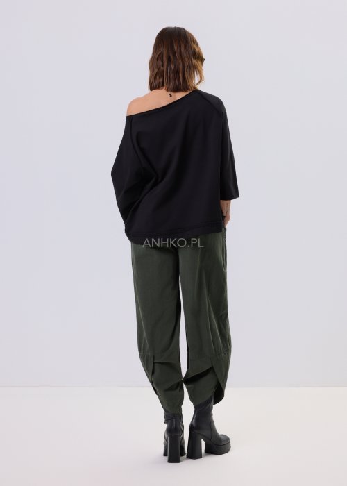 Czarna bluza damska o kroju oversize z raglanowymi rękawami, zestawiona z oliwkowymi spodniami i botkami w minimalistycznej, miejskiej stylizacji.