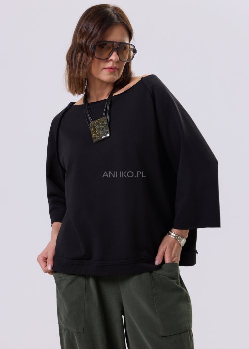 Czarna bluza damska o kroju oversize z raglanowymi rękawami, zestawiona z oliwkowymi spodniami i botkami w minimalistycznej, miejskiej stylizacji.