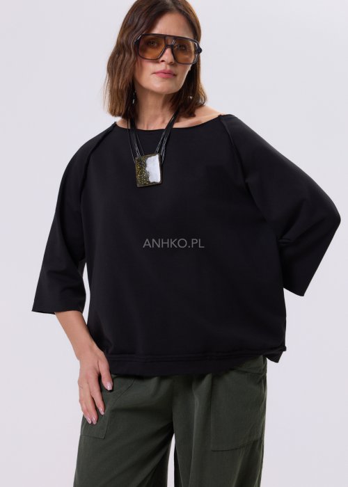 Czarna bluza damska o kroju oversize z raglanowymi rękawami, zestawiona z oliwkowymi spodniami i botkami w minimalistycznej, miejskiej stylizacji.