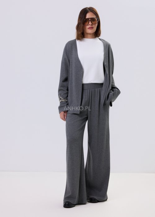 Szary komplet dzianinowy damski z luźnym kardiganem i szerokimi spodniami z wysokim stanem. Stylizacja z białym topem i czarnymi butami w minimalistycznym wydaniu.