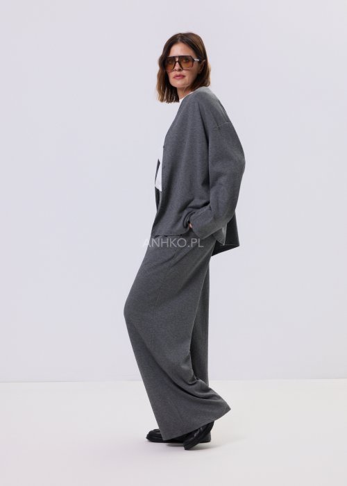 Szary komplet dzianinowy damski z luźnym kardiganem i szerokimi spodniami z wysokim stanem. Stylizacja z białym topem i czarnymi butami w minimalistycznym wydaniu.