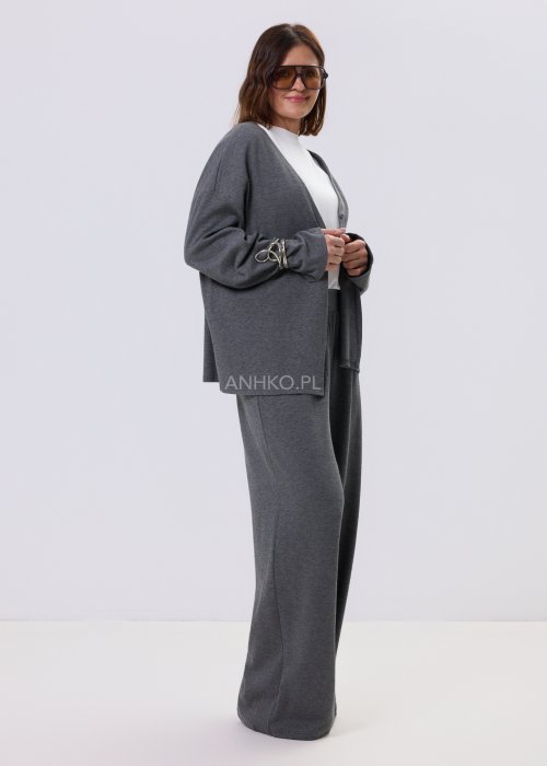 Szary komplet dzianinowy damski z luźnym kardiganem i szerokimi spodniami z wysokim stanem. Stylizacja z białym topem i czarnymi butami w minimalistycznym wydaniu.