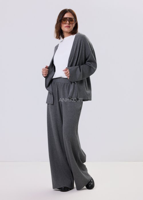 Szary komplet dzianinowy damski z luźnym kardiganem i szerokimi spodniami z wysokim stanem. Stylizacja z białym topem i czarnymi butami w minimalistycznym wydaniu.