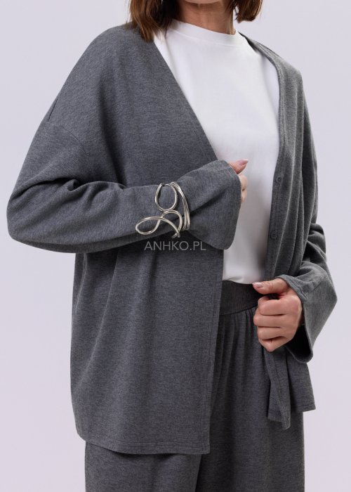 Szary komplet dzianinowy damski z luźnym kardiganem i szerokimi spodniami z wysokim stanem. Stylizacja z białym topem i czarnymi butami w minimalistycznym wydaniu.