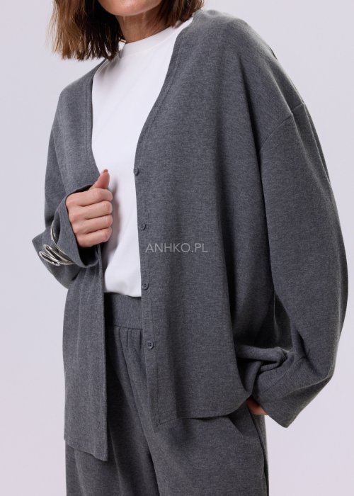 Szary komplet dzianinowy damski z luźnym kardiganem i szerokimi spodniami z wysokim stanem. Stylizacja z białym topem i czarnymi butami w minimalistycznym wydaniu.