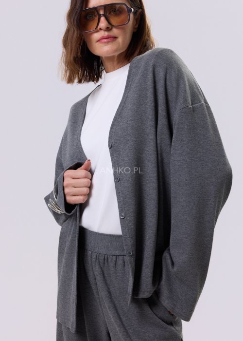 Szary komplet dzianinowy damski z luźnym kardiganem i szerokimi spodniami z wysokim stanem. Stylizacja z białym topem i czarnymi butami w minimalistycznym wydaniu.