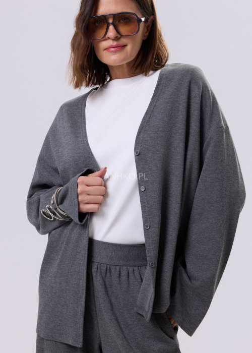 Szary komplet dzianinowy damski z luźnym kardiganem i szerokimi spodniami z wysokim stanem. Stylizacja z białym topem i czarnymi butami w minimalistycznym wydaniu.