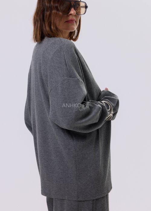 Szary komplet dzianinowy damski z luźnym kardiganem i szerokimi spodniami z wysokim stanem. Stylizacja z białym topem i czarnymi butami w minimalistycznym wydaniu.