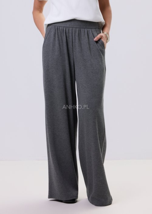 Szary komplet dzianinowy damski z luźnym kardiganem i szerokimi spodniami z wysokim stanem. Stylizacja z białym topem i czarnymi butami w minimalistycznym wydaniu.