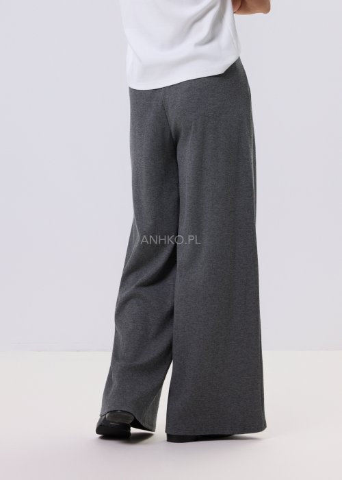 Szary komplet dzianinowy damski z luźnym kardiganem i szerokimi spodniami z wysokim stanem. Stylizacja z białym topem i czarnymi butami w minimalistycznym wydaniu.