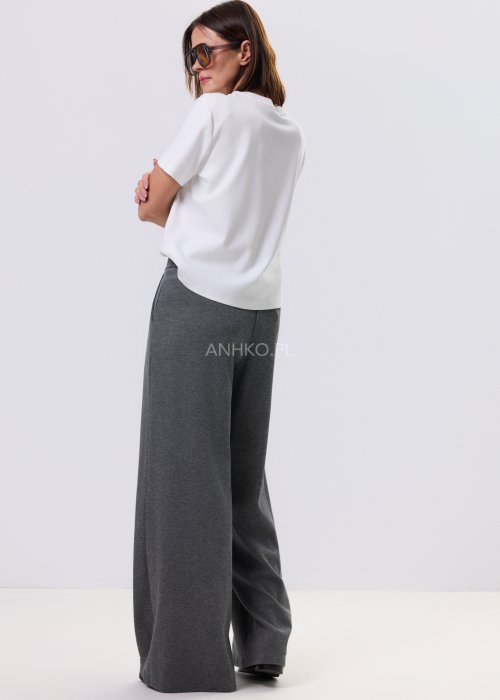 Szary komplet dzianinowy damski z luźnym kardiganem i szerokimi spodniami z wysokim stanem. Stylizacja z białym topem i czarnymi butami w minimalistycznym wydaniu.