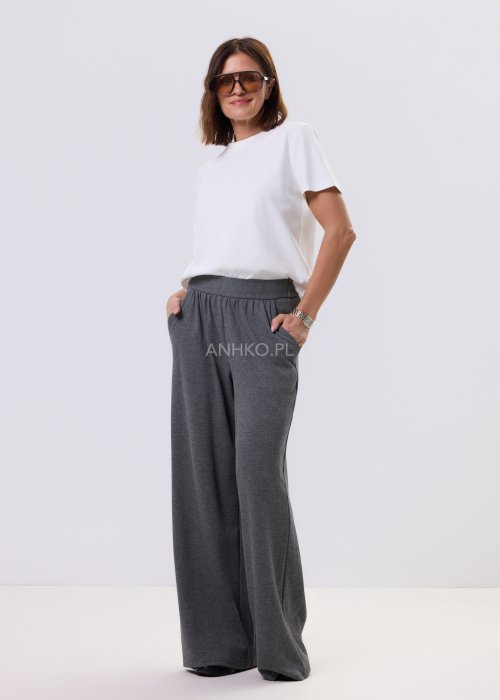 Szary komplet dzianinowy damski z luźnym kardiganem i szerokimi spodniami z wysokim stanem. Stylizacja z białym topem i czarnymi butami w minimalistycznym wydaniu.