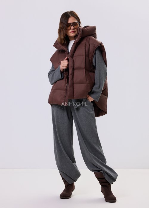 Brązowa kamizelka puchowa z kapturem i pikowaniem, zestawiona z szarym kompletem dresowym w miejskiej, casualowej stylizacji.