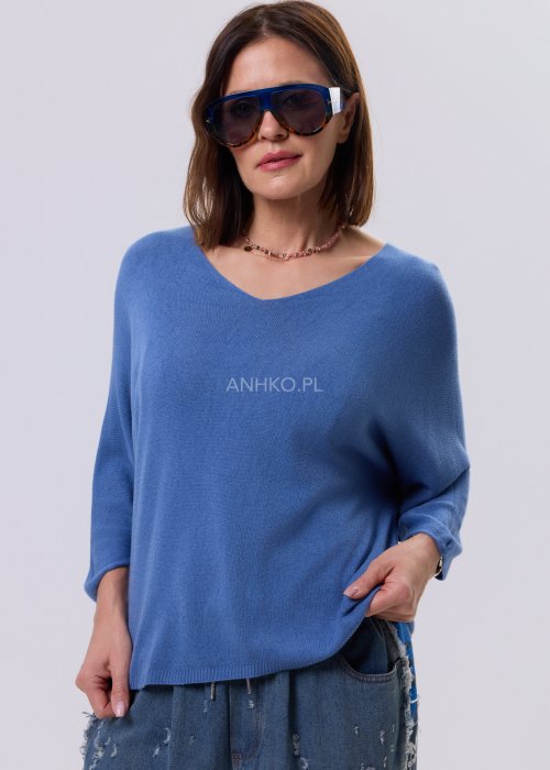 Niebieski sweter damski o nietoperzowym kroju z dekoltem V i rękawem 3/4, zestawiony z luźnymi jeansami i trampkami w casualowej stylizacji.