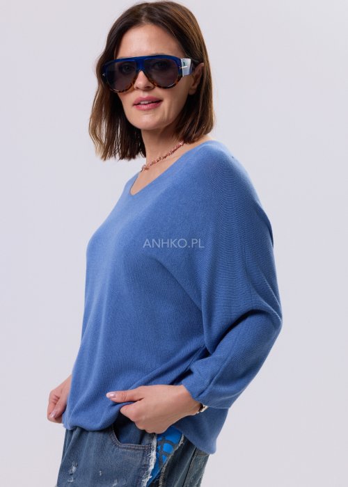 Niebieski sweter damski o nietoperzowym kroju z dekoltem V i rękawem 3/4, zestawiony z luźnymi jeansami i trampkami w casualowej stylizacji.