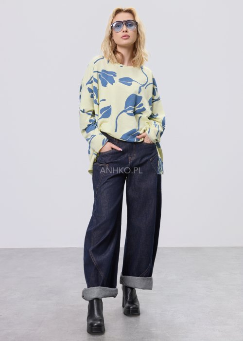 Żółta bluza damska oversize z niebieskim, graficznym wzorem roślinnym, luźny fason w stylizacji z ciemnymi jeansami.