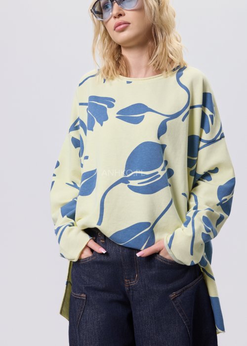 Żółta bluza damska oversize z niebieskim, graficznym wzorem roślinnym, luźny fason w stylizacji z ciemnymi jeansami.