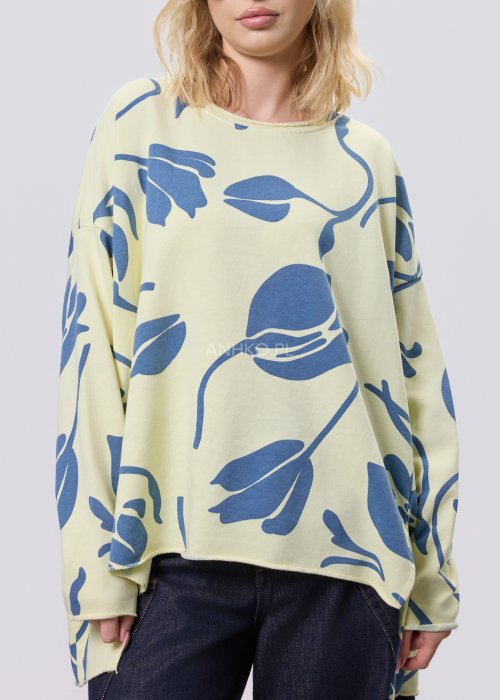 Żółta bluza damska oversize z niebieskim, graficznym wzorem roślinnym, luźny fason w stylizacji z ciemnymi jeansami.