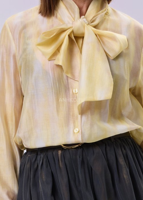 Masełkowa elegancka bluzka z wiązaną kokardą przy szyi i długim rękawem. Stylizacja z czarną spódnicą i paskiem podkreślającym talię.