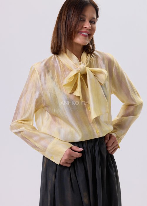 Masełkowa elegancka bluzka z wiązaną kokardą przy szyi i długim rękawem. Stylizacja z czarną spódnicą i paskiem podkreślającym talię.