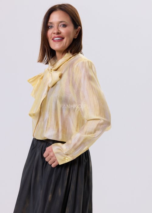 Masełkowa elegancka bluzka z wiązaną kokardą przy szyi i długim rękawem. Stylizacja z czarną spódnicą i paskiem podkreślającym talię.