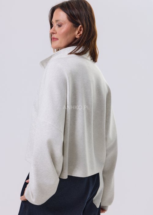 Jasnoszara damska bluza oversize z krótkim fasonem i stójką zapinaną na suwak, zestawiona z ciemnymi spodniami o szerokiej nogawce.