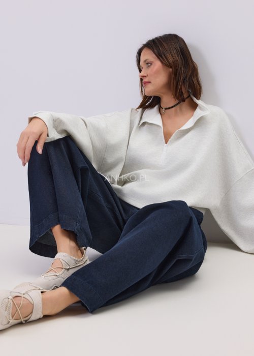 Jasnoszara damska bluza oversize z krótkim fasonem i stójką zapinaną na suwak, zestawiona z ciemnymi spodniami o szerokiej nogawce.