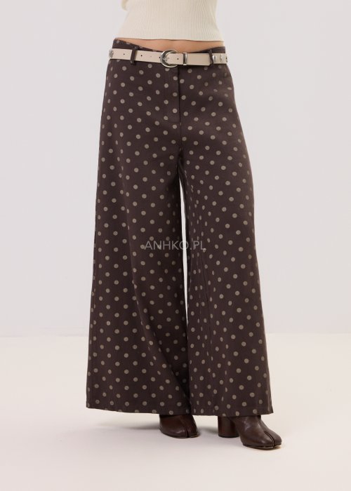 Brązowe damskie spodnie Retro Dots z szeroką nogawką, ozdobione beżowymi groszkami. Model z wysokim stanem i paskiem w talii, w stylizacji z kremowym topem oraz brązowymi botkami.