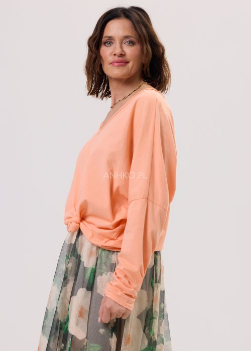 Brzoskwiniowa bluzka damska Anio o luźnym, oversize’owym fasonie z dekoltem V i długim rękawem, zestawiona ze zwiewną spódnicą w kwiaty w kobiecej stylizacji.
