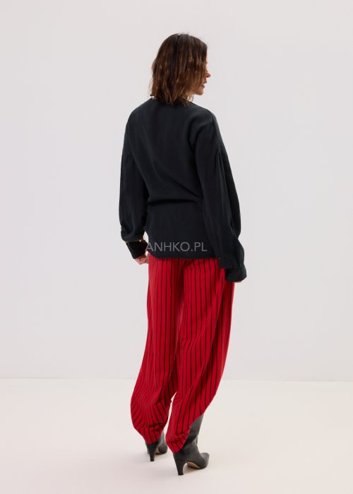 Czerwone spodnie damskie w czarne pionowe paski o szerokim kroju, zestawione z czarną bluzą i botkami na obcasie w nowoczesnej stylizacji.
