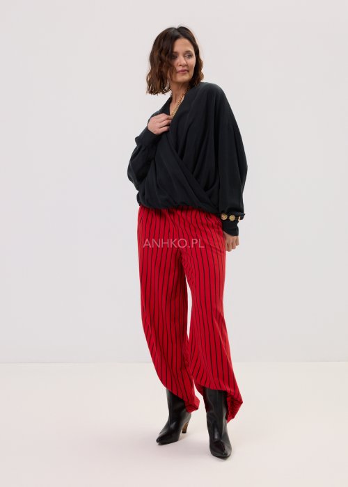 Czerwone spodnie damskie w czarne pionowe paski o szerokim kroju, zestawione z czarną bluzą i botkami na obcasie w nowoczesnej stylizacji.