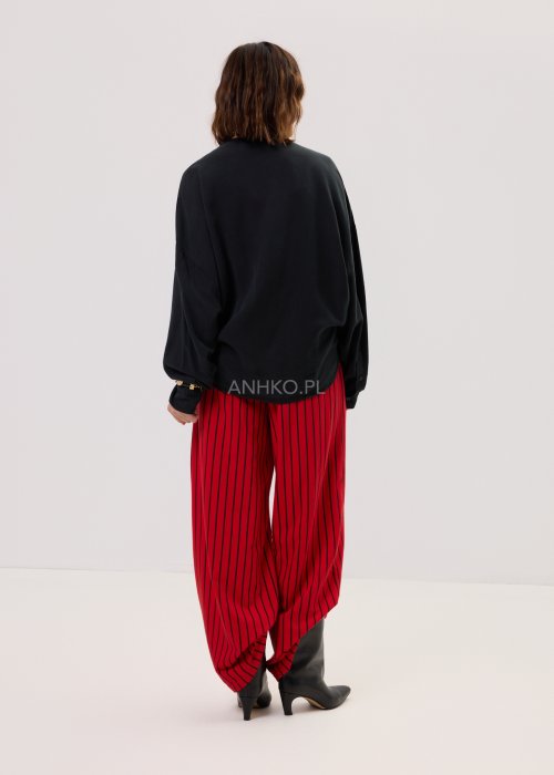 Czerwone spodnie damskie w czarne pionowe paski o szerokim kroju, zestawione z czarną bluzą i botkami na obcasie w nowoczesnej stylizacji.