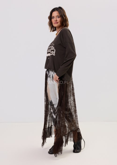 Damskie spodnie w odcieniach brązu i beżu, z nałożoną koronkową warstwą z ciemnobrązowej siateczki, stylizowane z brązowymi mokasynami i skarpetkami.