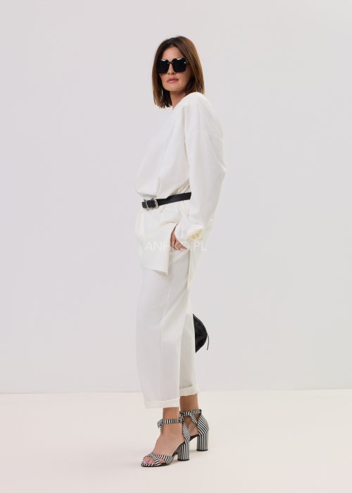 Białe spodnie Starola Rose z podwiniętą nogawką i eleganckim paskiem, luźny fason z zakładkami z przodu, w stylizacji z sandałami na słupku w czarno-białe paski.