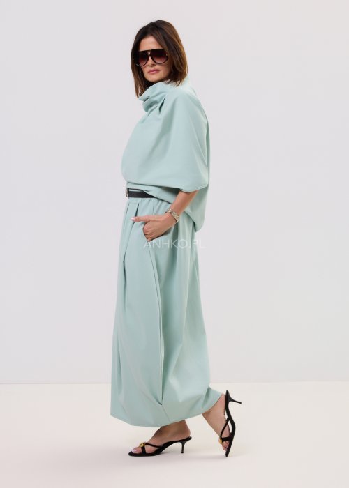 Miętowa damska bluzka o luźnym kroju z krótkim rękawem, szerokim dekoltem typu woda i dekoracyjnymi zakładkami z przodu.