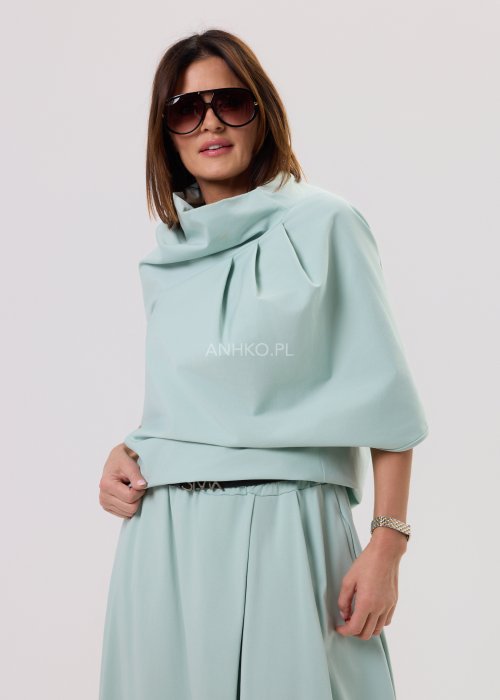 Miętowa damska bluzka o luźnym kroju z krótkim rękawem, szerokim dekoltem typu woda i dekoracyjnymi zakładkami z przodu.