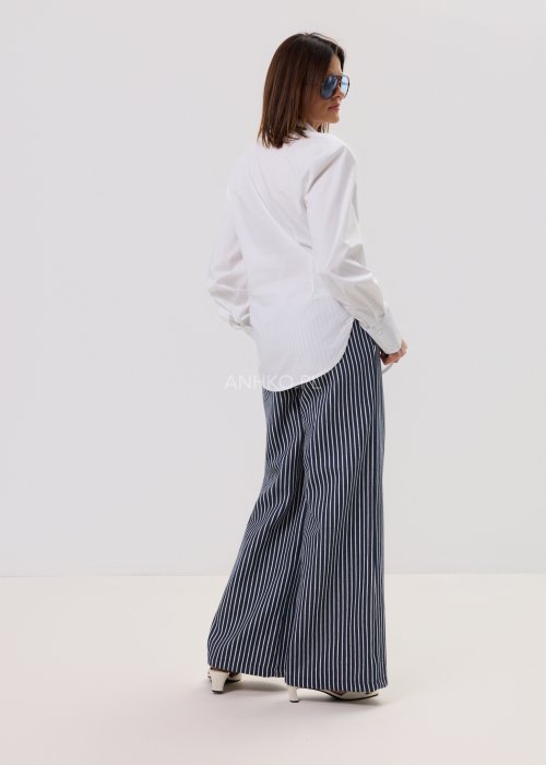 Biała koszula damska o klasycznym kroju z kołnierzykiem, zapinana na guziki, z długimi rękawami zakończonymi mankietami; delikatnie taliowana