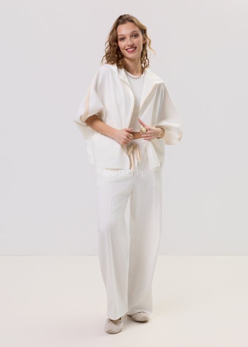 Damska kremowa bluza oversize z kapturem zapinana na zamek, szerokie rękawy, duża kieszeń z przodu – stylizacja z jasnymi spodniami.