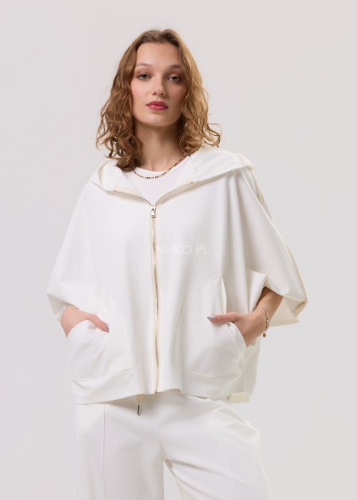 Damska kremowa bluza oversize z kapturem zapinana na zamek, szerokie rękawy, duża kieszeń z przodu – stylizacja z jasnymi spodniami.