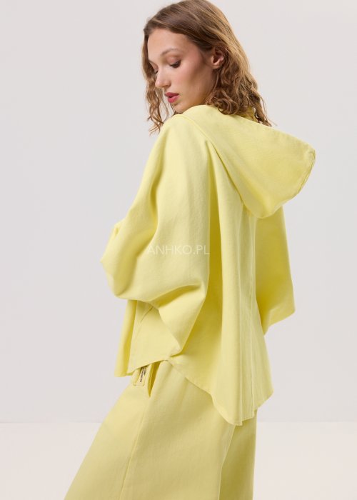 Żółta kurtka damska z kapturem zapinana na zamek, o luźnym kroju z szerokimi rękawami, w lekkim stylu casual.